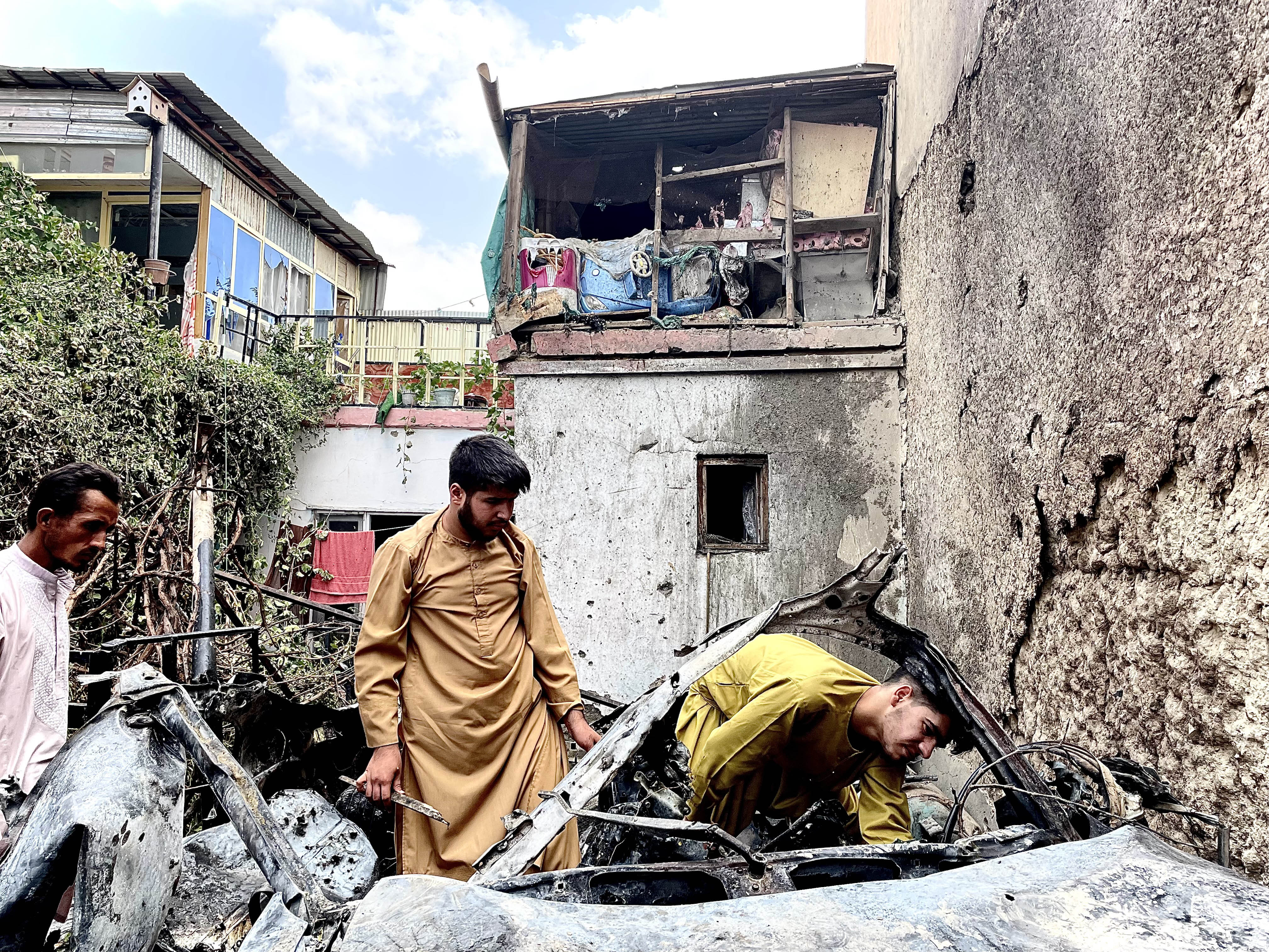 Men search the car hit by a US drone strike in Kabul on Aug. 29, 2021.